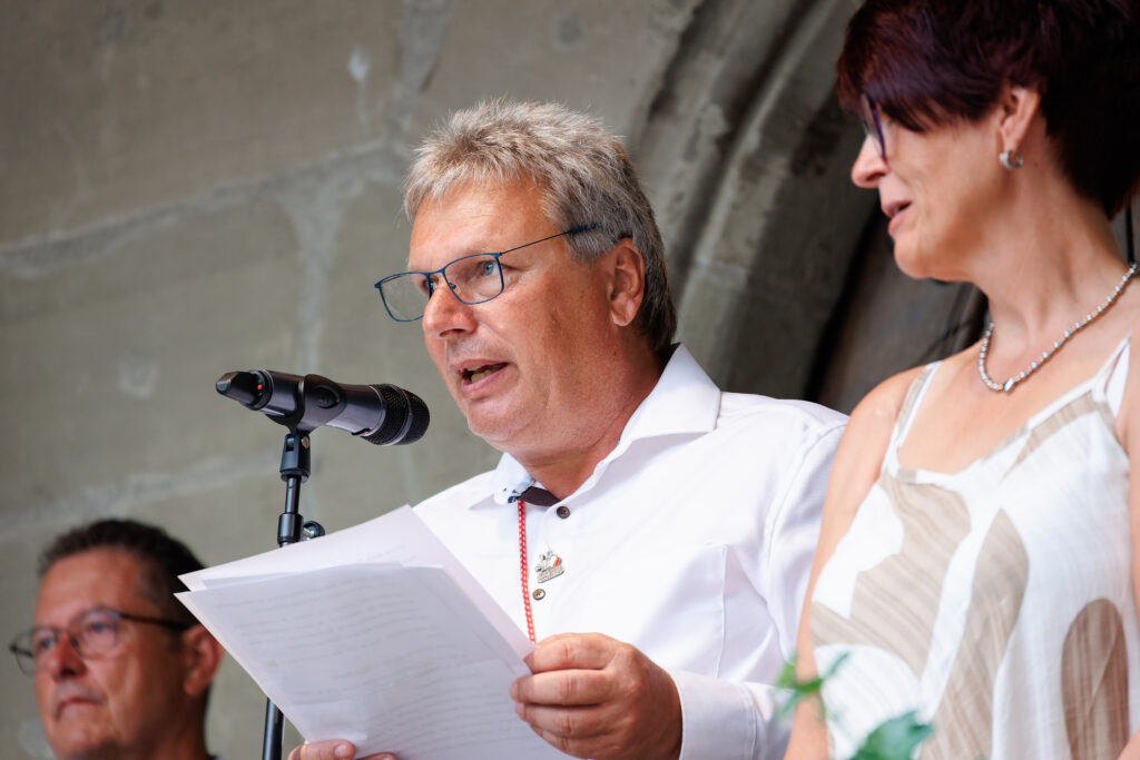 Homme à lunettes lisant un discours au microphone en plein air
