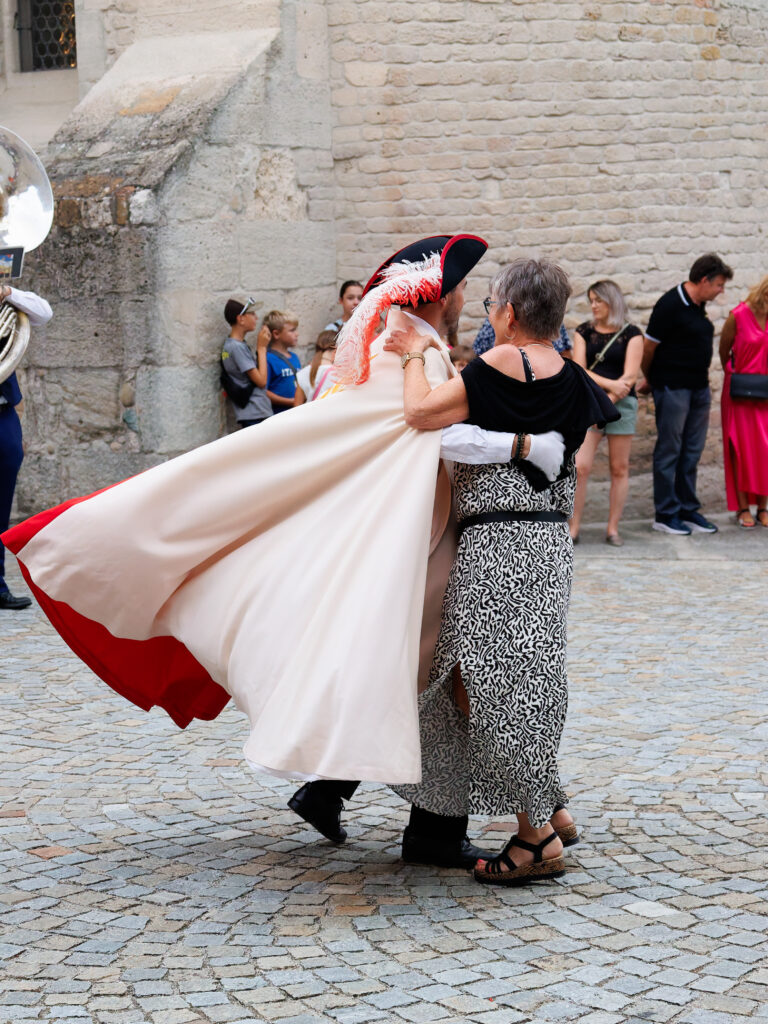 Personnage costumé dansant avec une femme sur une place pavée