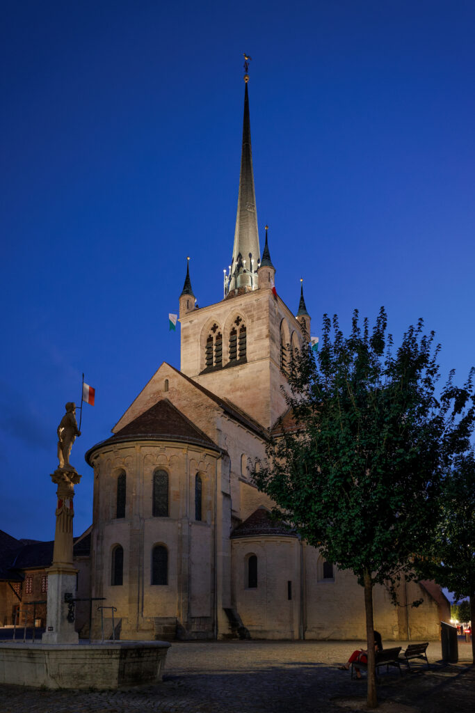 Église médiévale illuminée la nuit avec clocher élancé et statue
