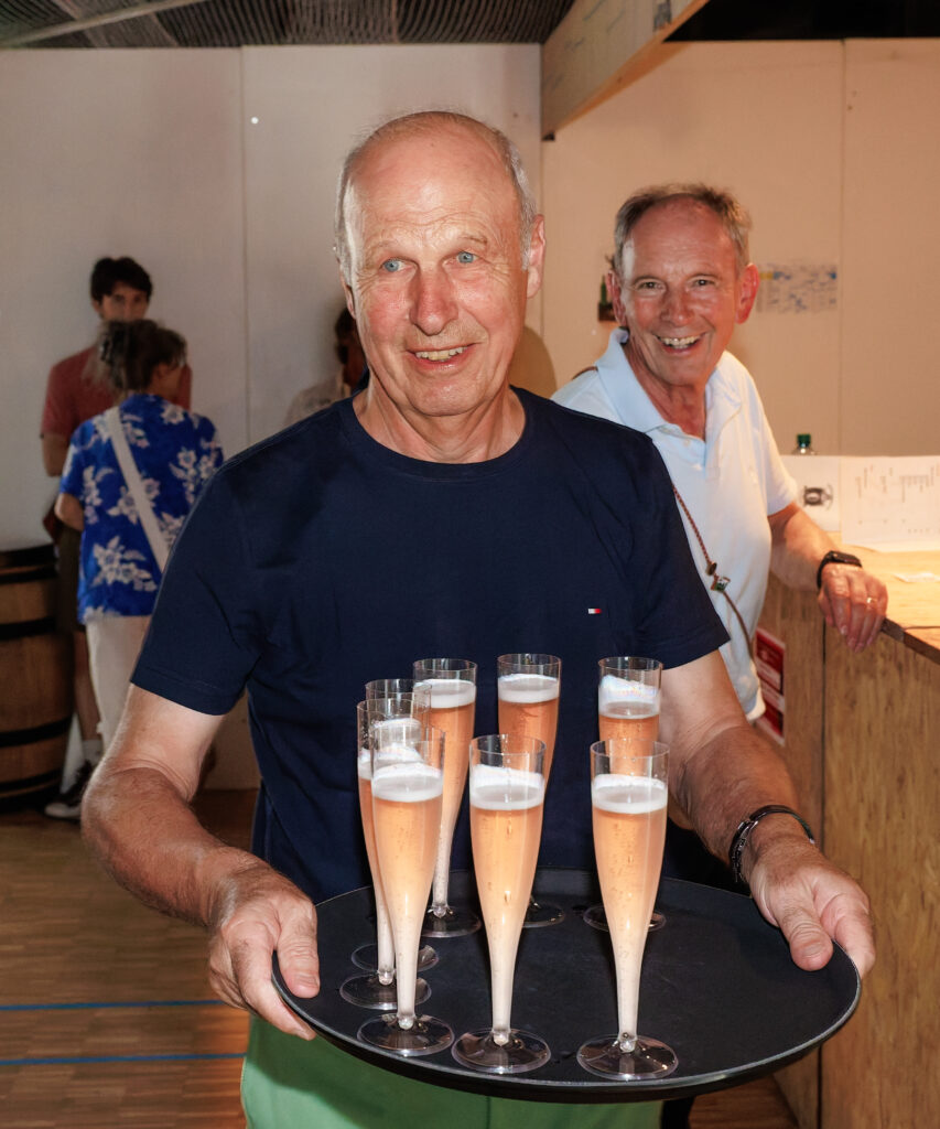 Homme souriant portant un plateau de flûtes de champagne rosé