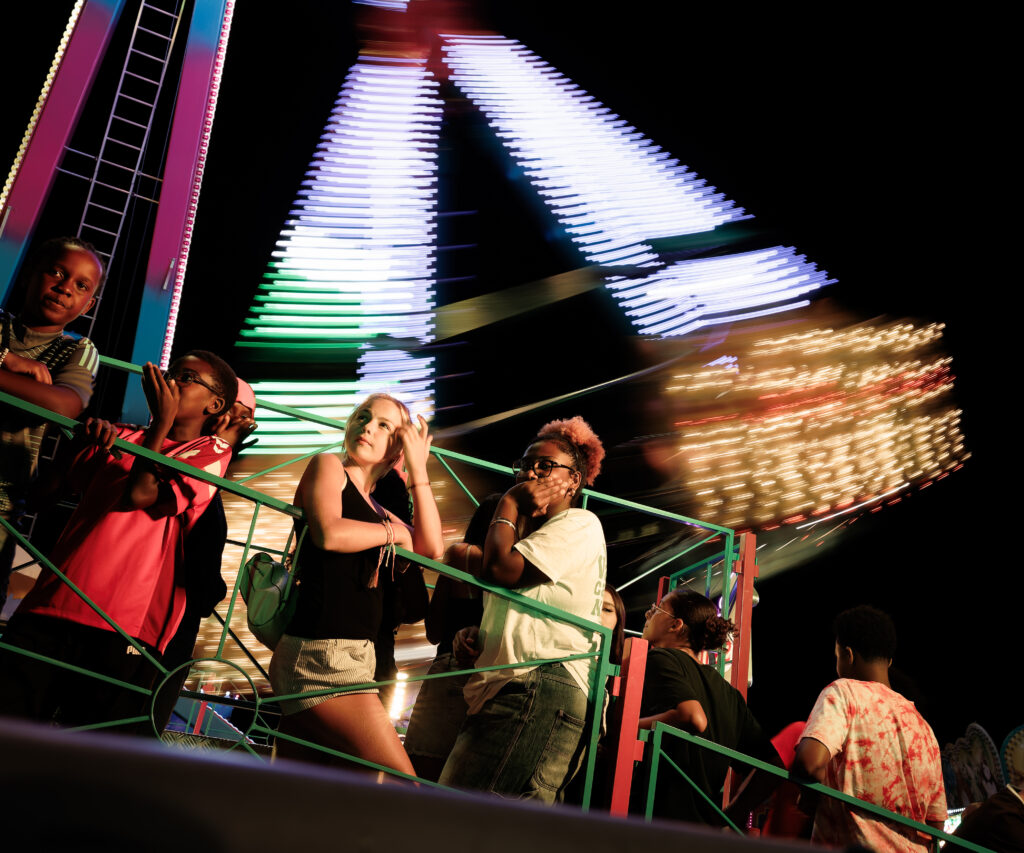 Jeunes visiteurs devant un manège lumineux en fête foraine nocturne